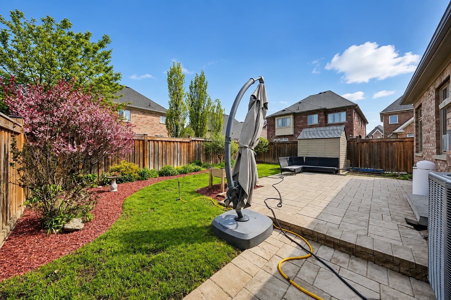 Backyard listing photo before AI furniture removal — umbrella & hoses still in the room